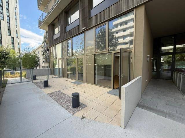 Ebenerdige Terrasse mit Fliesen und Kiesflächen vor großen Glasfronten eines modernen Gebäudes.