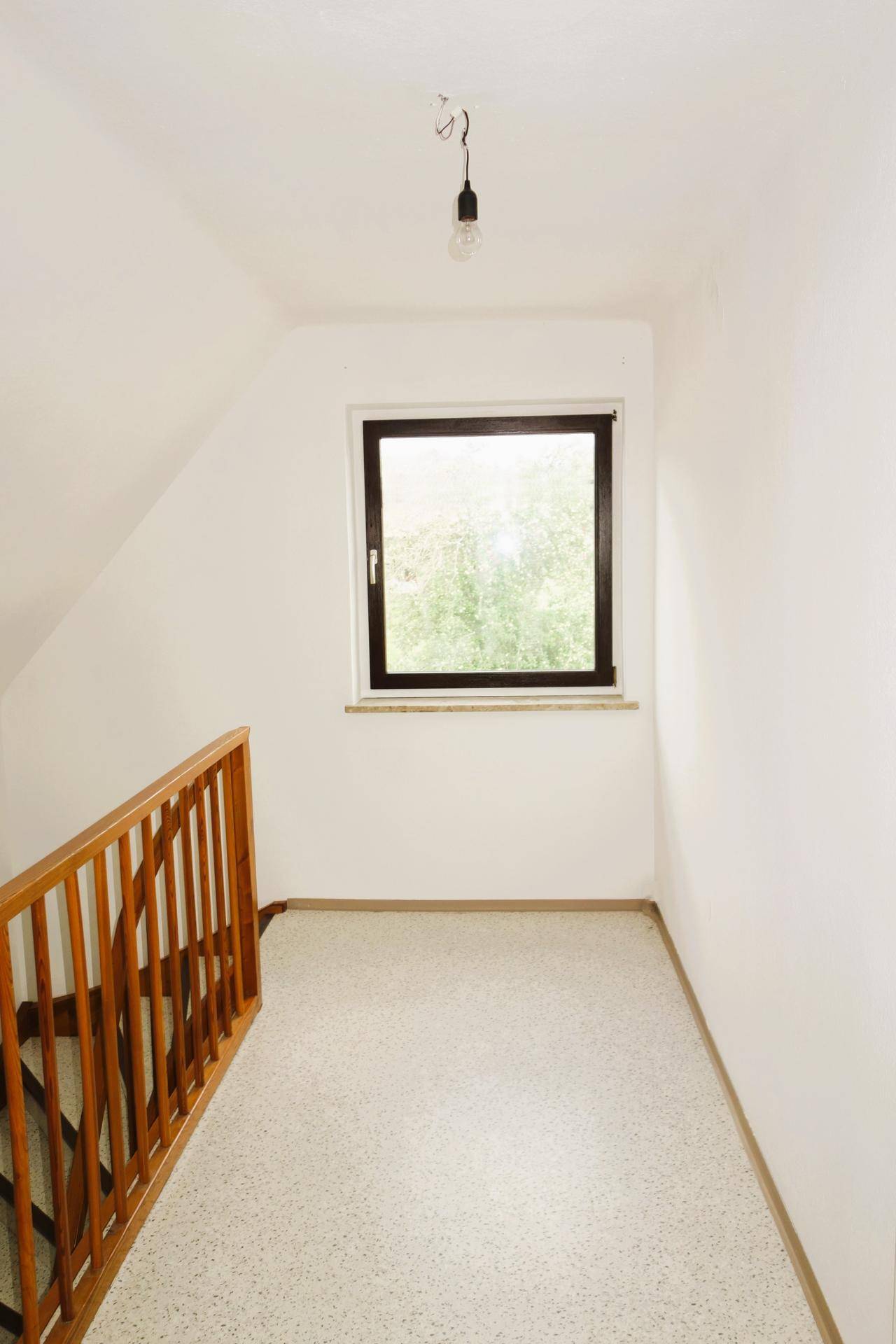 Heller Flur im Obergeschoss mit Dachschräge, Fenster und Holzgeländer.