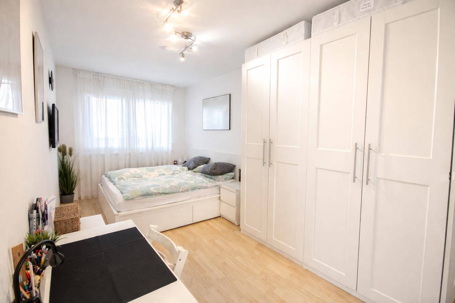 Schlafzimmer mit Doppelbett, großem Kleiderschrank und Schreibtisch, hell und funktional.