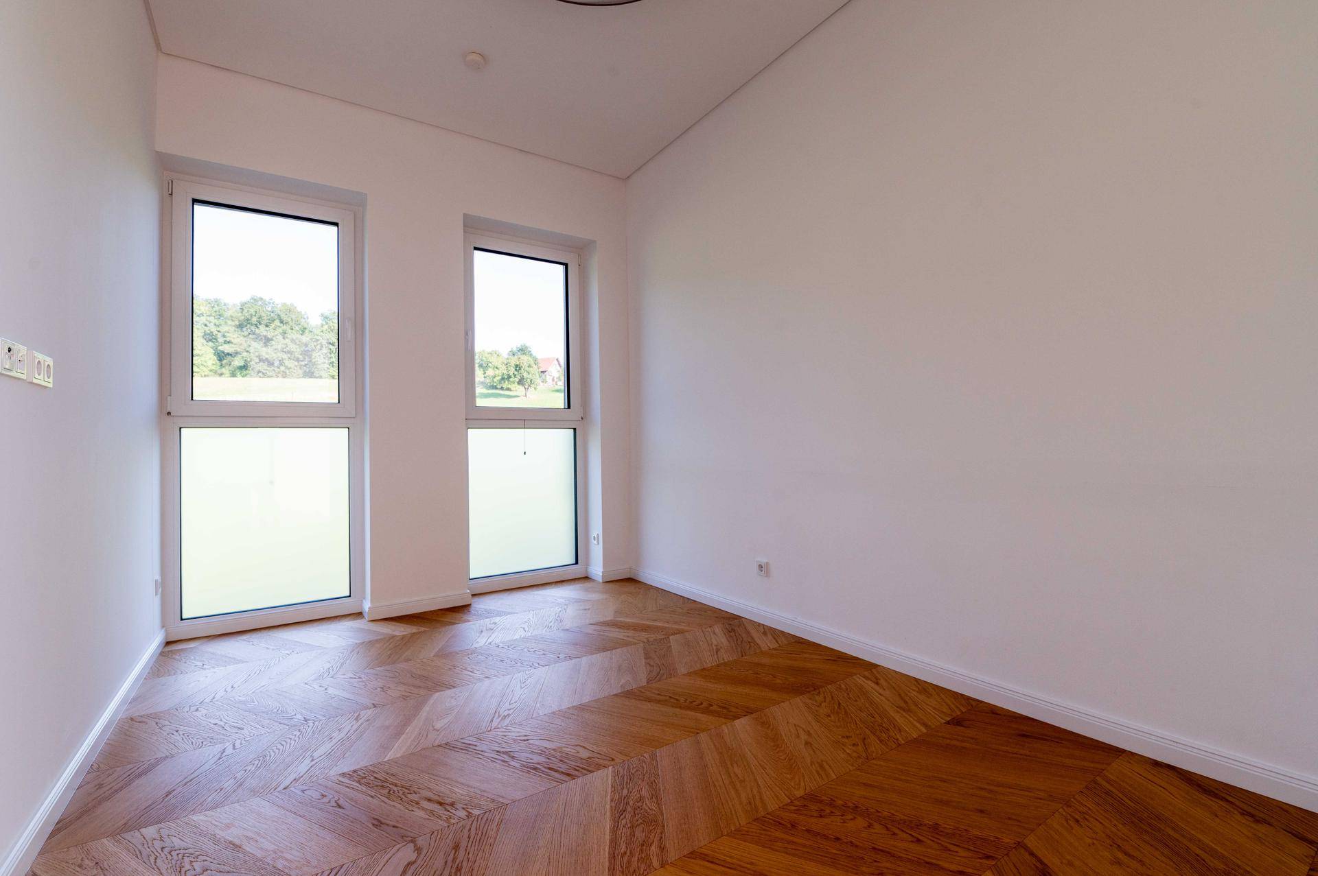 Geräumiges Schlafzimmer mit Fischgrätparkett und viel Tageslicht durch die Fenster.