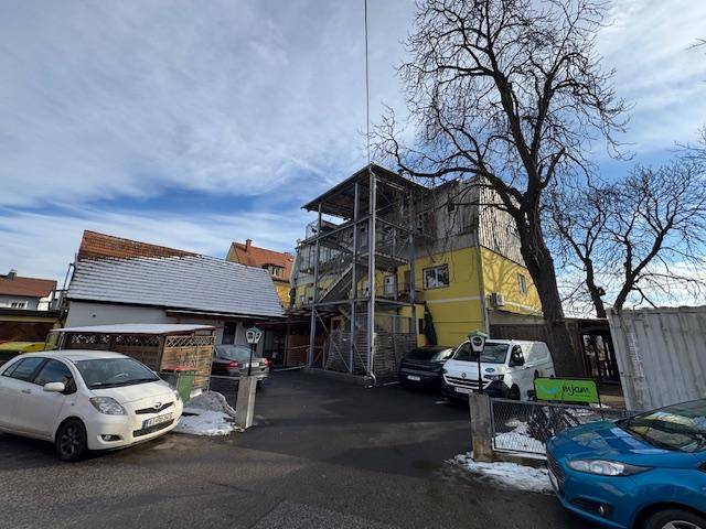 Rückansicht des Gebäudes mit externer Metalltreppe, Parkplätzen und kahlen Bäumen im Winter.