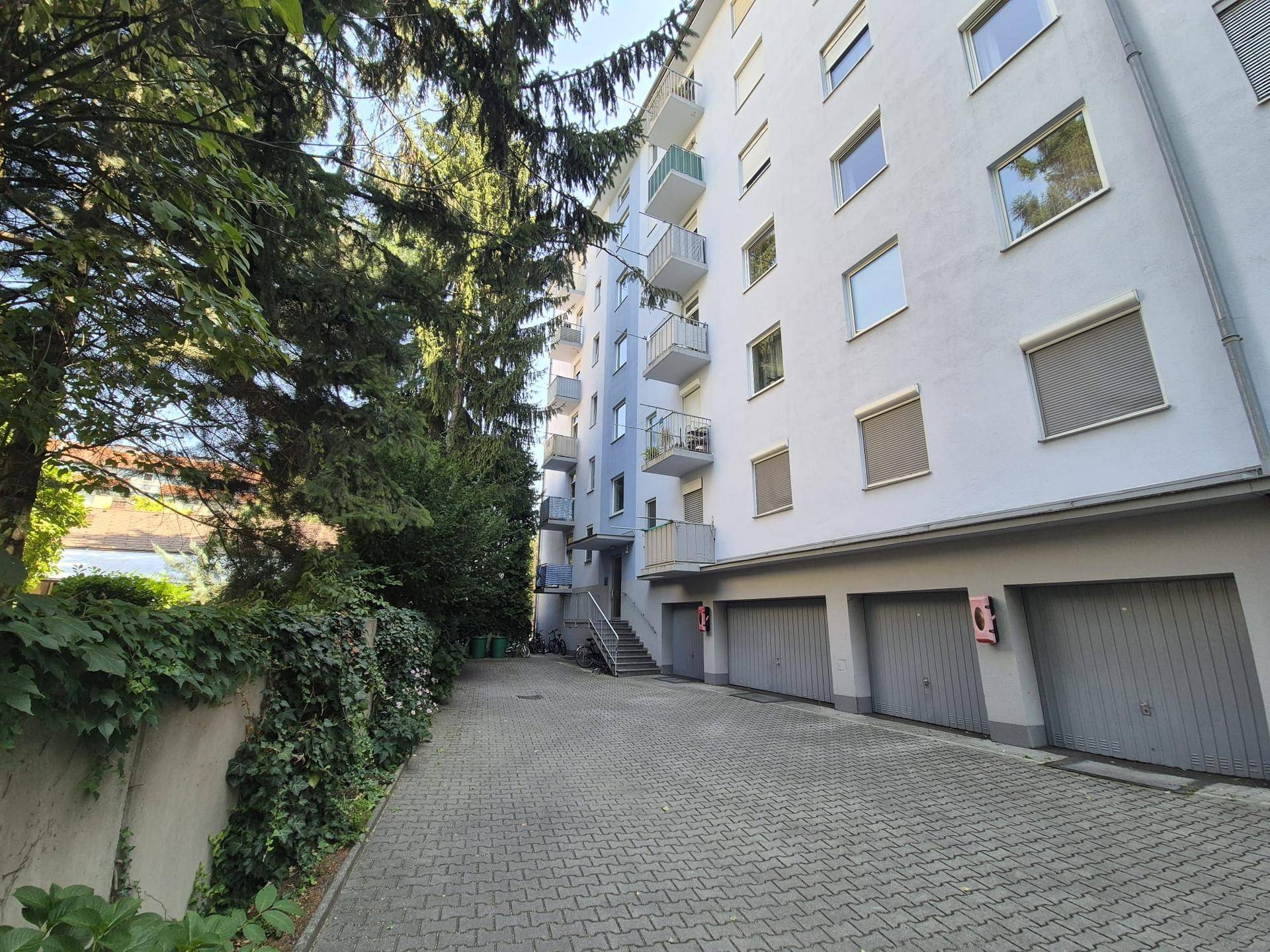 Außenansicht eines Mehrfamilienhauses mit Garagen und begrüntem Zugangsbereich.
