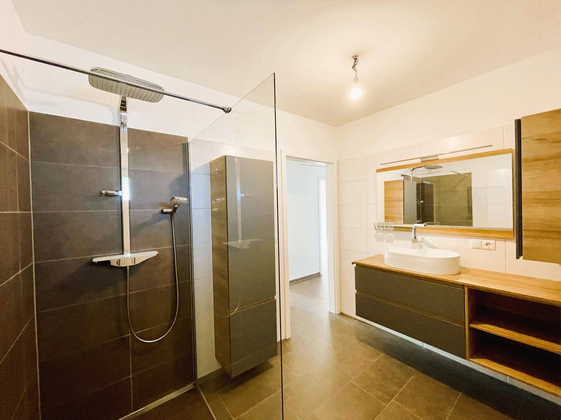 Geräumiges Badezimmer mit begehbarer Dusche, Regendusche und modernem Waschtisch.