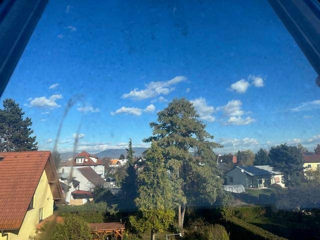 Weitblick aus dem Fenster über Häuser, Bäume und Berge unter blauem Himmel.