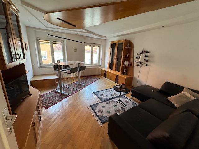 Helles Wohnzimmer mit Holzboden, dunklem Sofa und einem Bartisch unter einer Holzdecke.