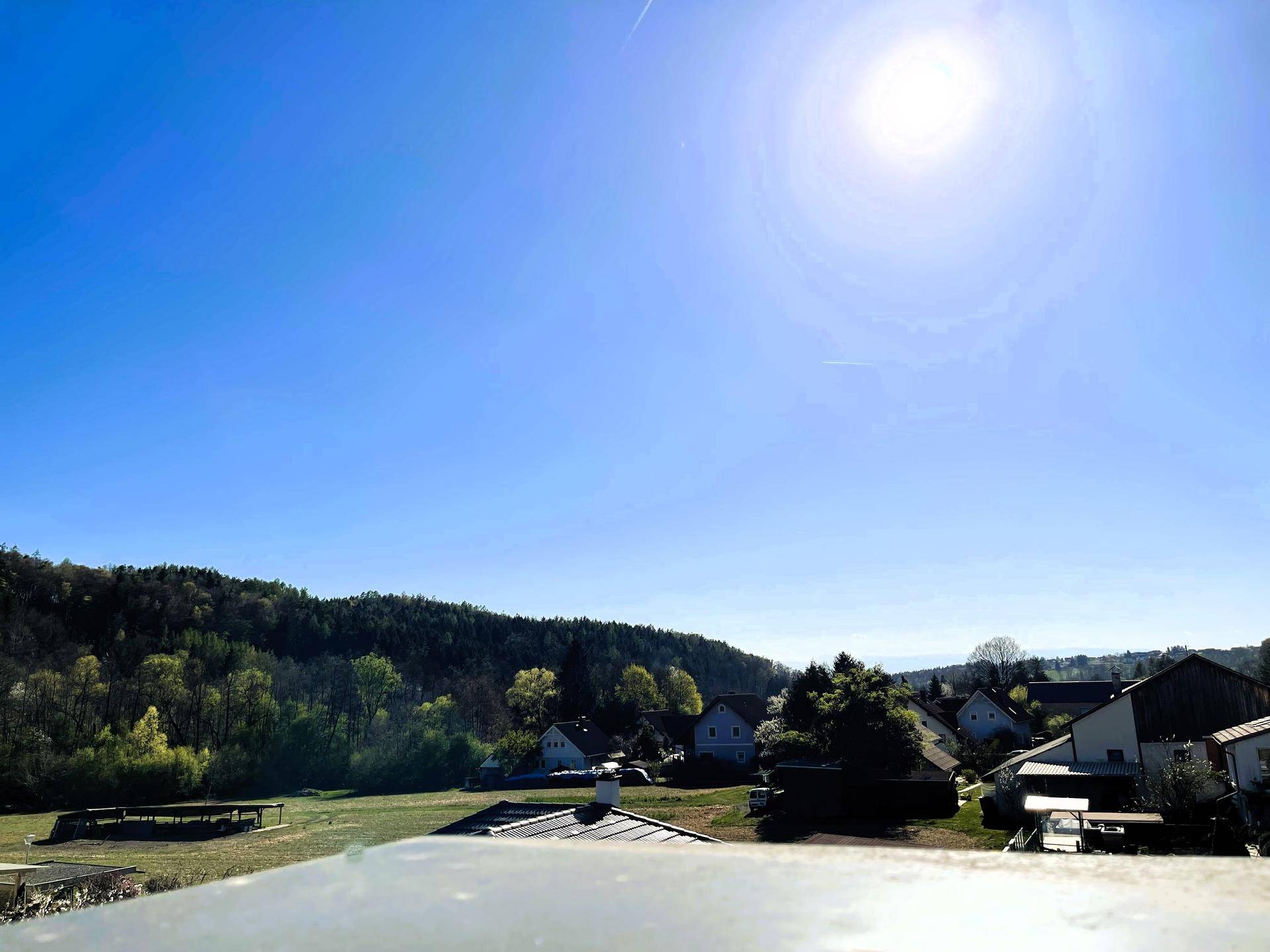 Weitläufiger Panoramablick über grüne Hügel und eine ländliche Wohnsiedlung unter blauem Himmel.