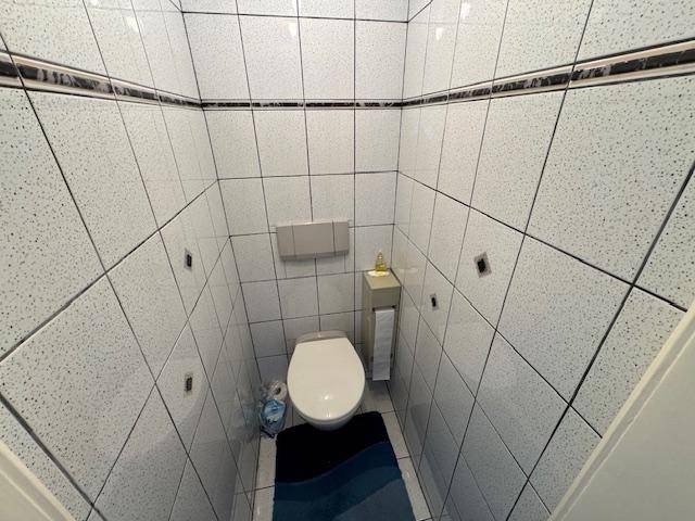 Kleines Gäste-WC mit wandhängender Toilette und hellen Fliesen an Wänden und Boden.