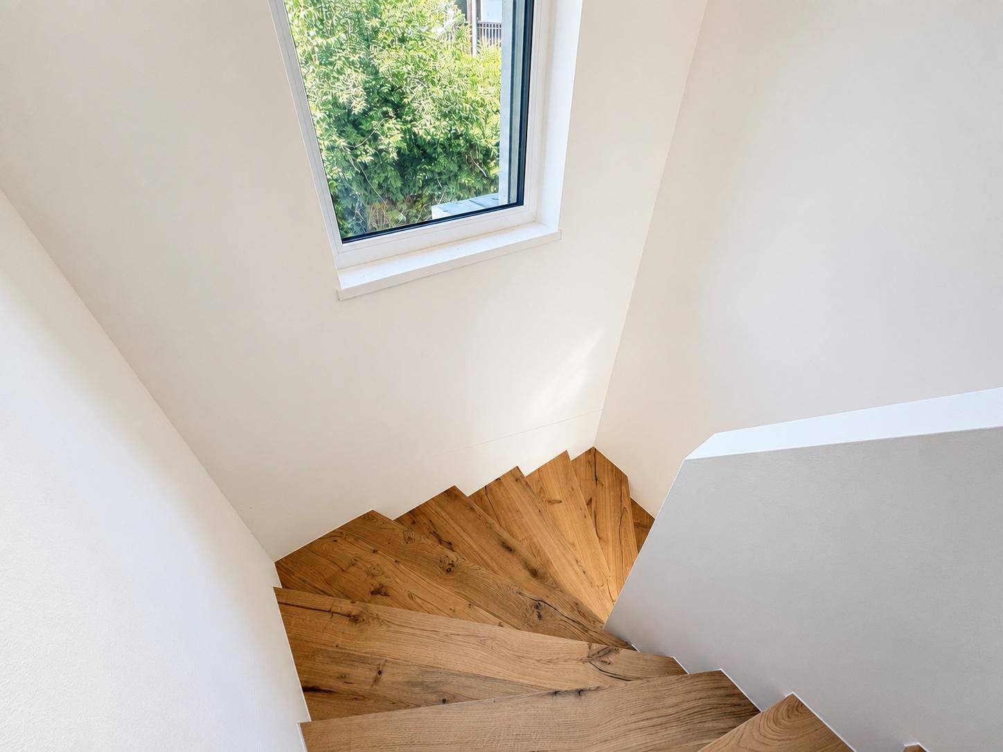 Blick von oben auf die moderne Holztreppe mit einem Fenster, das den Treppenaufgang erhellt.