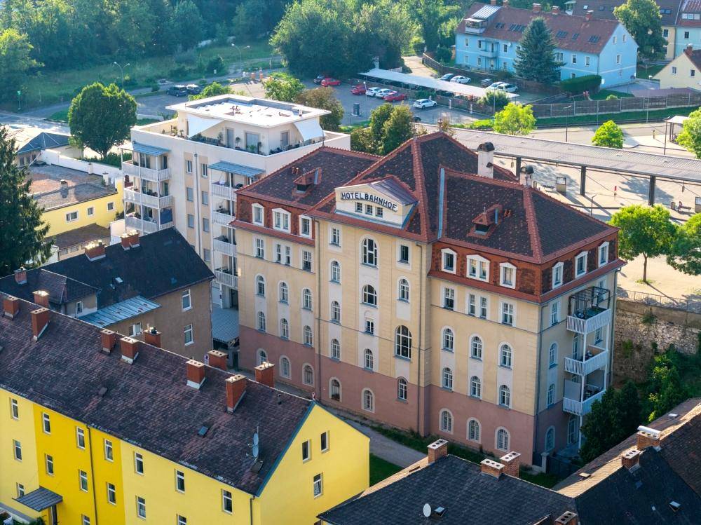 Luftaufnahme eines historischen Hotels und eines modernen Wohngebäudes in städtischer Umgebung.