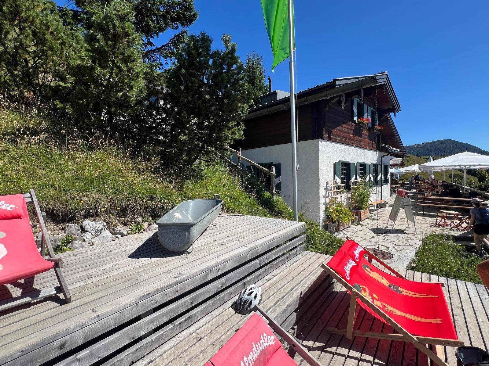 Gemütliche Holzterrasse mit Liegestühlen vor einer traditionellen Berghütte und sonnigem Himmel.