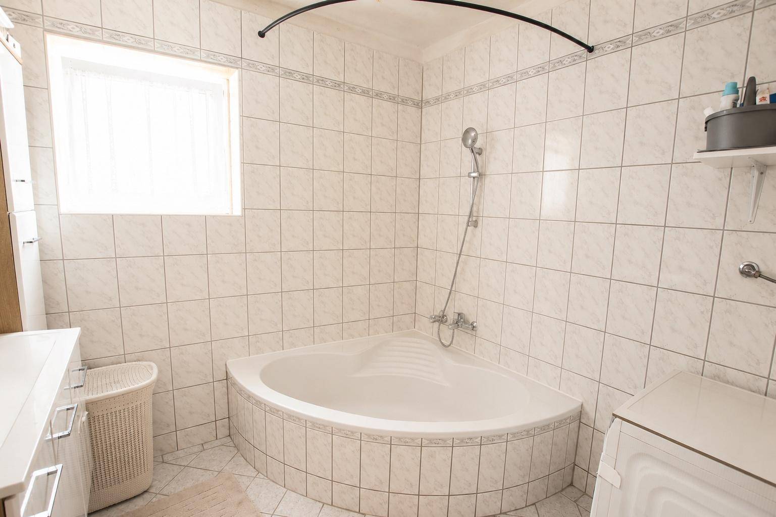 Badezimmer mit Eckbadewanne, Duschvorrichtung und hellen Fliesen.