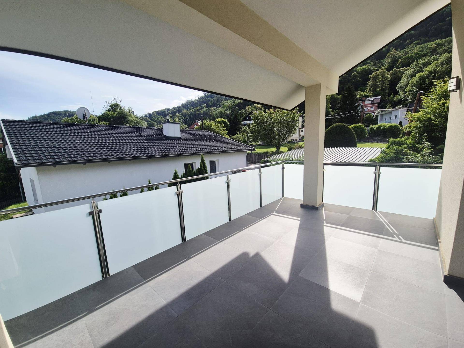 Geräumiger Balkon mit Glasgeländer und weitem Blick auf die grüne Umgebung.