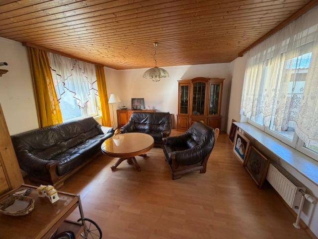 Geräumiges Wohnzimmer mit Holzboden, Holzdecke und Ledersofas, gut beleuchtet.
