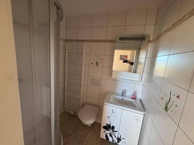 Kleines Badezimmer mit Dusche, WC, Waschbecken und weißen Fliesen mit floralen Akzenten.
