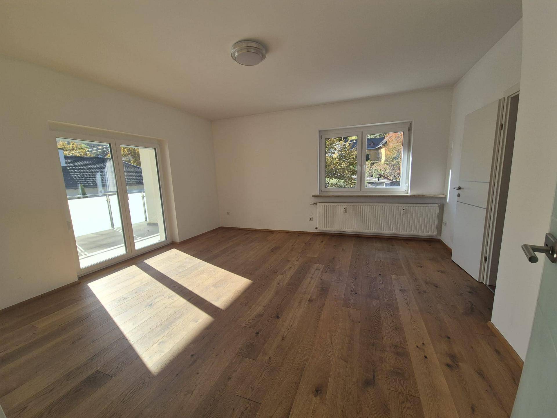 Helles Zimmer mit Holzboden und großem Schiebetürzugang zu einem Balkon oder einer Terrasse.