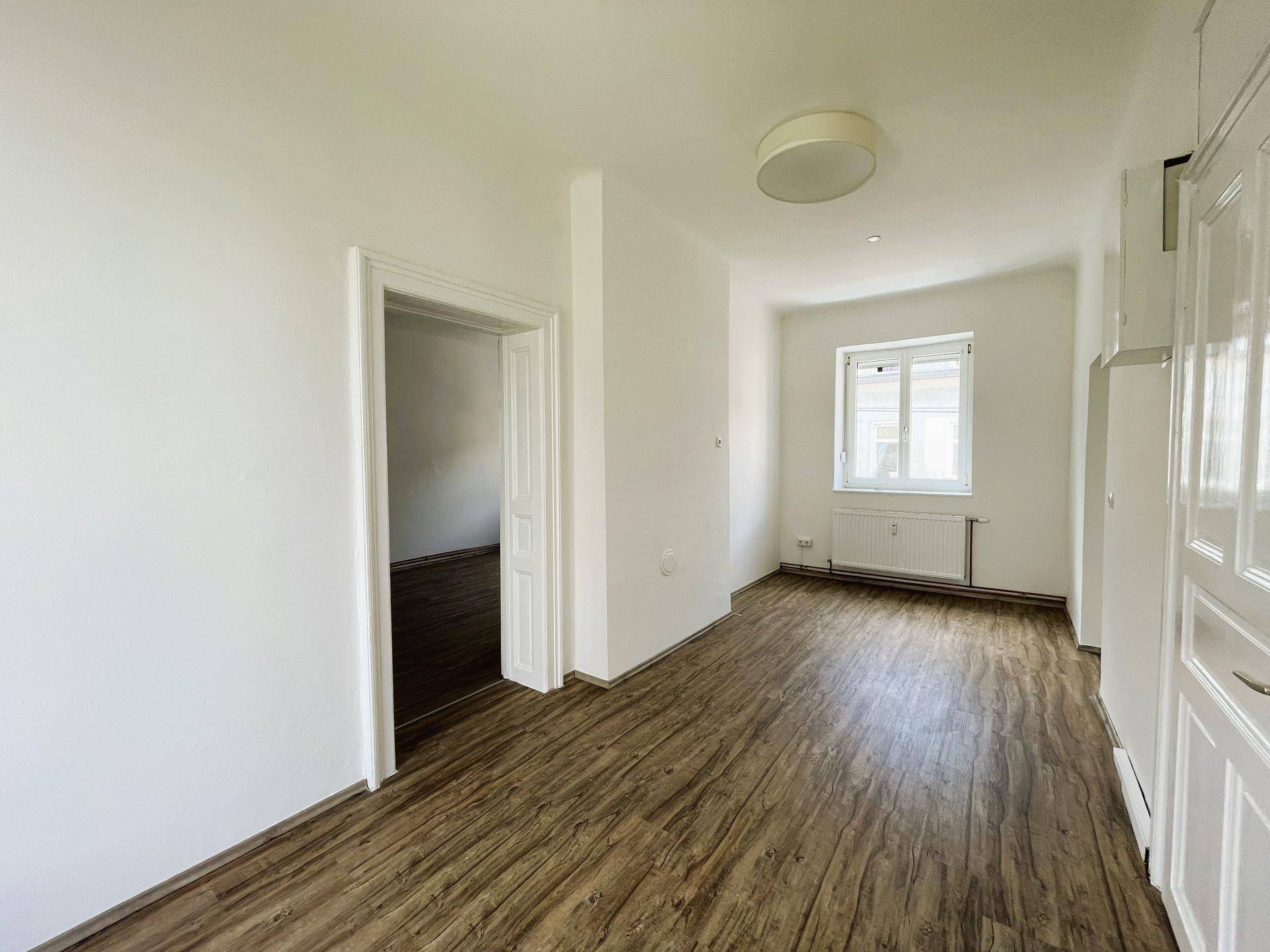 Heller Flur mit Laminatboden, einem Fenster und integrierten Schränken, der zu weiteren Räumen führt.
