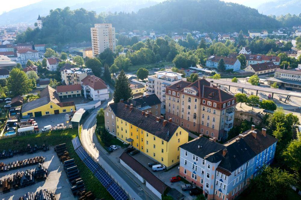 Weitläufige Luftaufnahme einer Stadt mit Bergen im Hintergrund und verschiedenen Gebäudetypen.