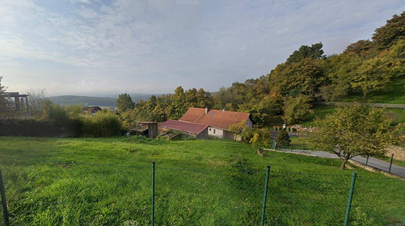 Weitläufiges grünes Grundstück mit Blick auf ein traditionelles Haus und bewaldete Hügel in der Ferne.