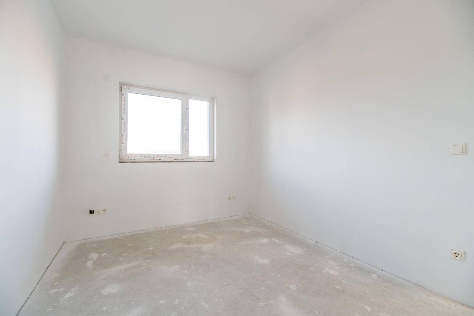 Helles Schlafzimmer im Rohbau mit weiß gestrichenen Wänden und einem Fenster.