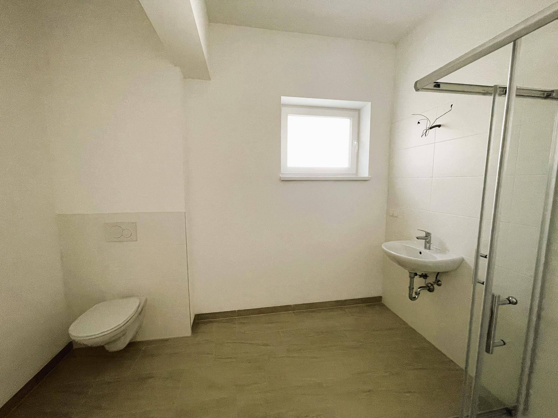 Modernes Badezimmer mit Dusche, WC, Waschbecken und einem Fenster für natürliche Belüftung.