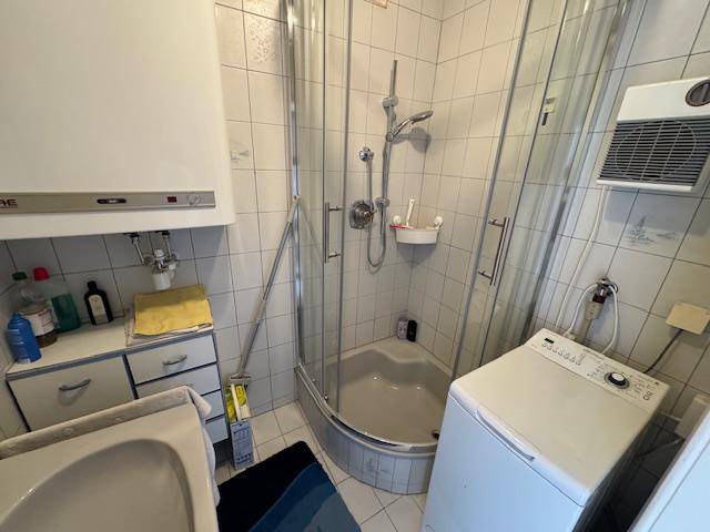 Badezimmer mit Eckdusche, Waschbecken und Waschmaschine, komplett gefliest.