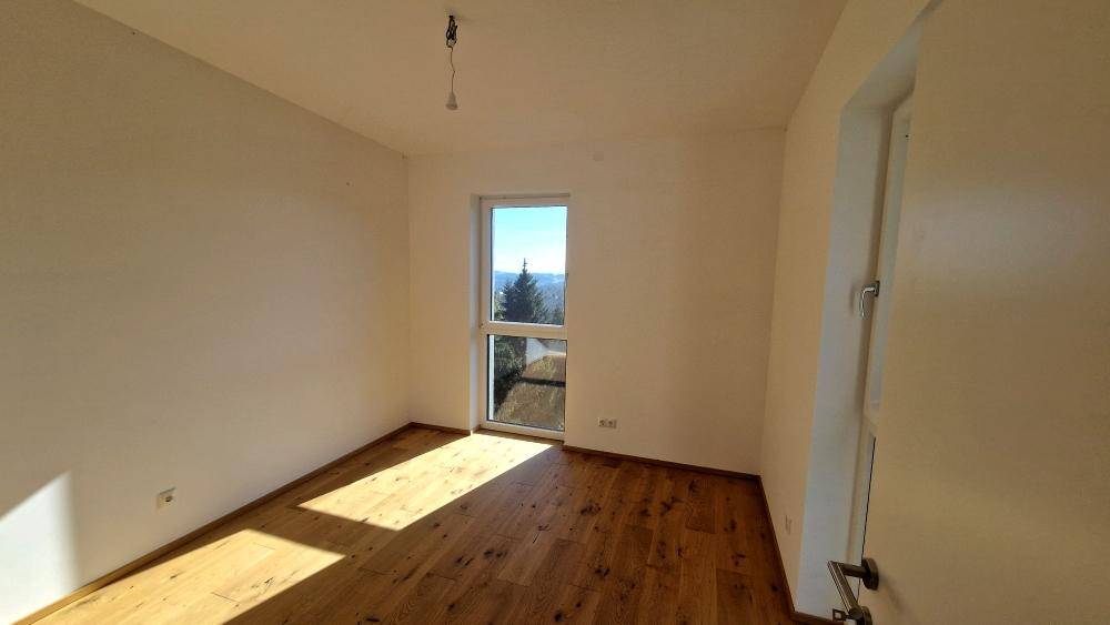 Helles Schlafzimmer mit Holzboden und weitem Ausblick durch das Fenster.