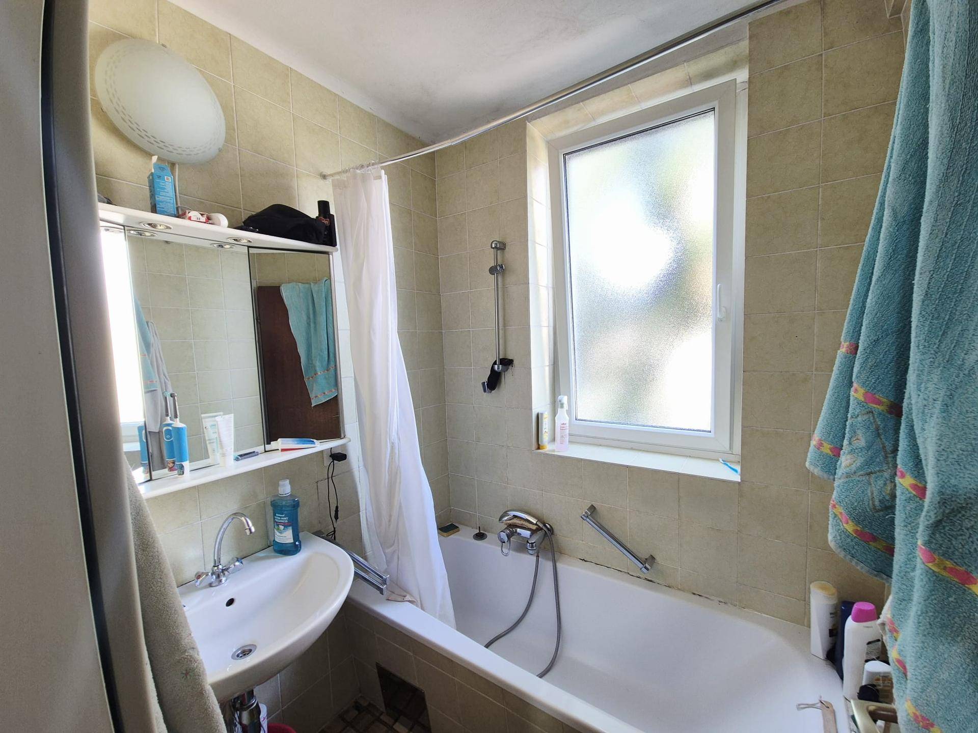 Badezimmer mit Badewanne, Waschbecken, Spiegelschrank und Fenster für Tageslicht.