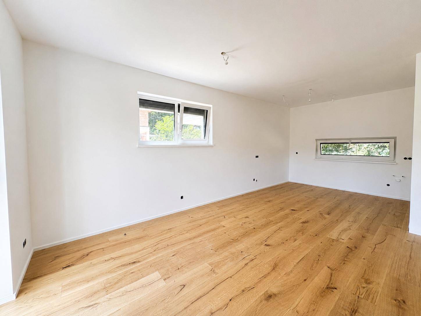Heller Raum mit Holzboden, weißen Wänden und zwei Fenstern, bereit für die individuelle Gestaltung.