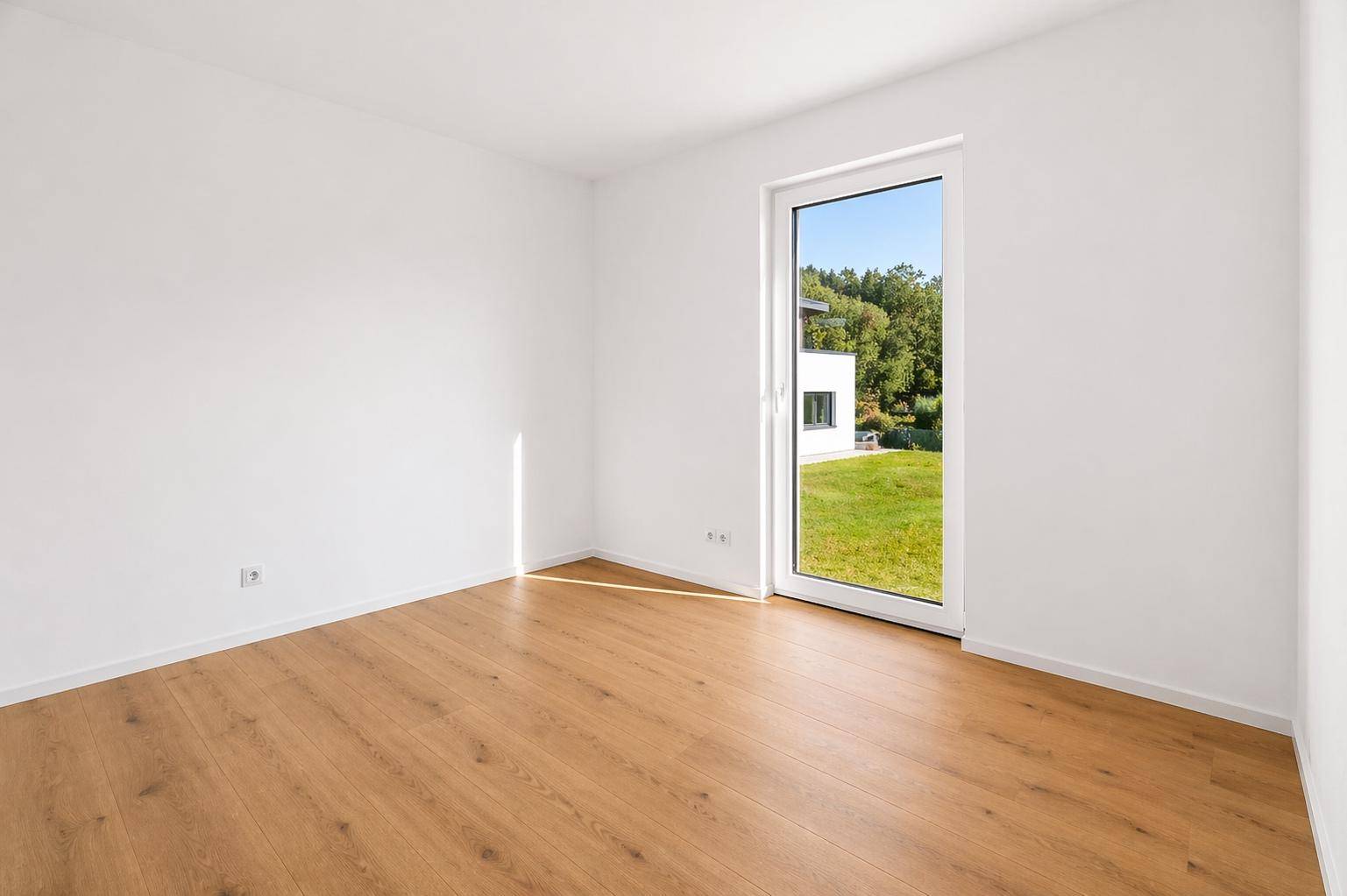 Helles Schlafzimmer mit Holzboden und bodentiefem Fenster mit Blick ins Grüne.