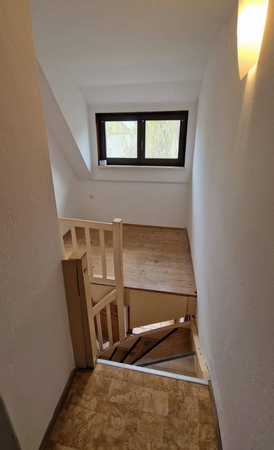 Holztreppe führt hinauf zu einem hellen Dachzimmer mit Fenster.