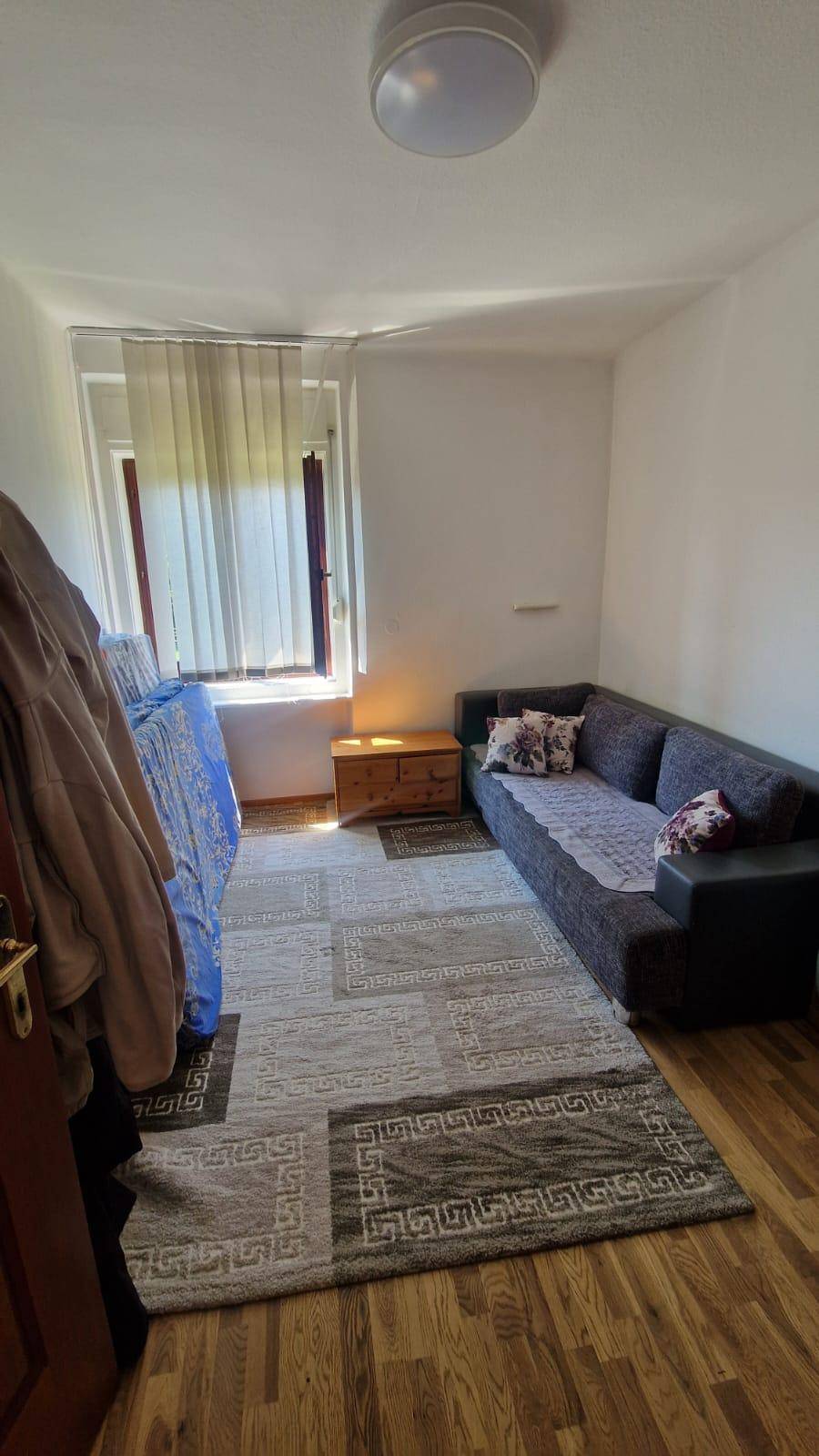 Gemütliches Zimmer mit Holzboden, Sofa und Fenster, das als Wohn- oder Gästezimmer genutzt werden kann.