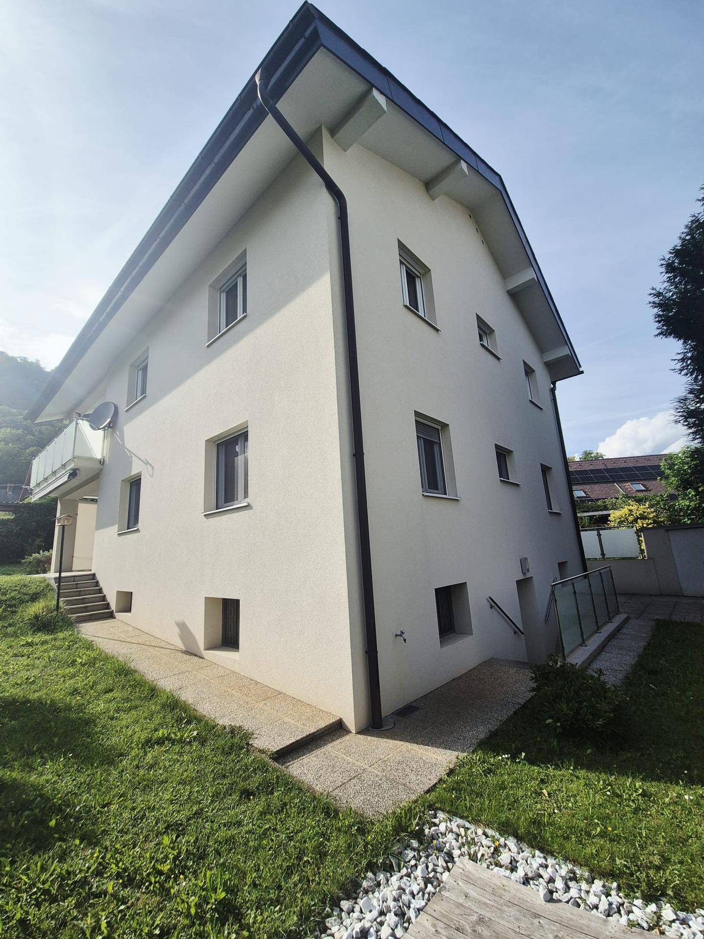 Seitenansicht des Hauses mit hellen Fassaden und Zugang zum Gartenbereich.