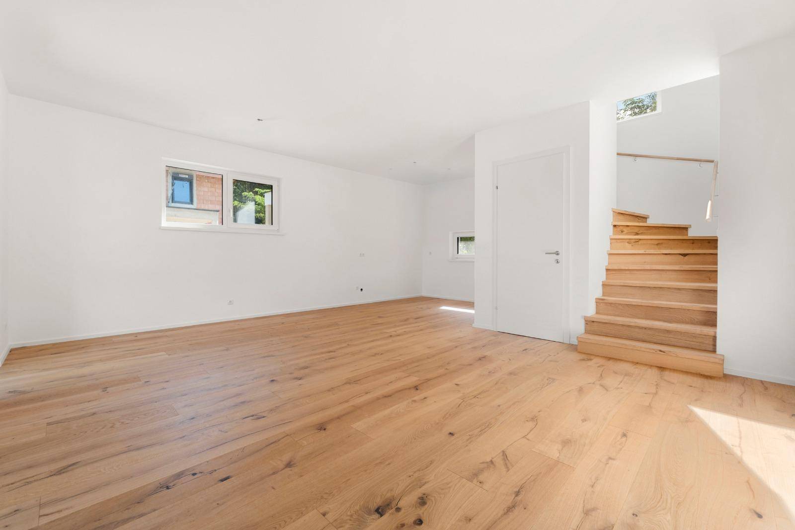 Geräumiges Wohnzimmer mit hellem Eichenparkett und offener Holztreppe.