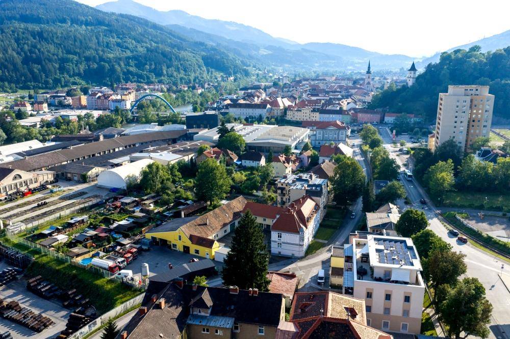 Weitläufige Luftaufnahme einer Stadt mit Bergen im Hintergrund und Flusslandschaft.