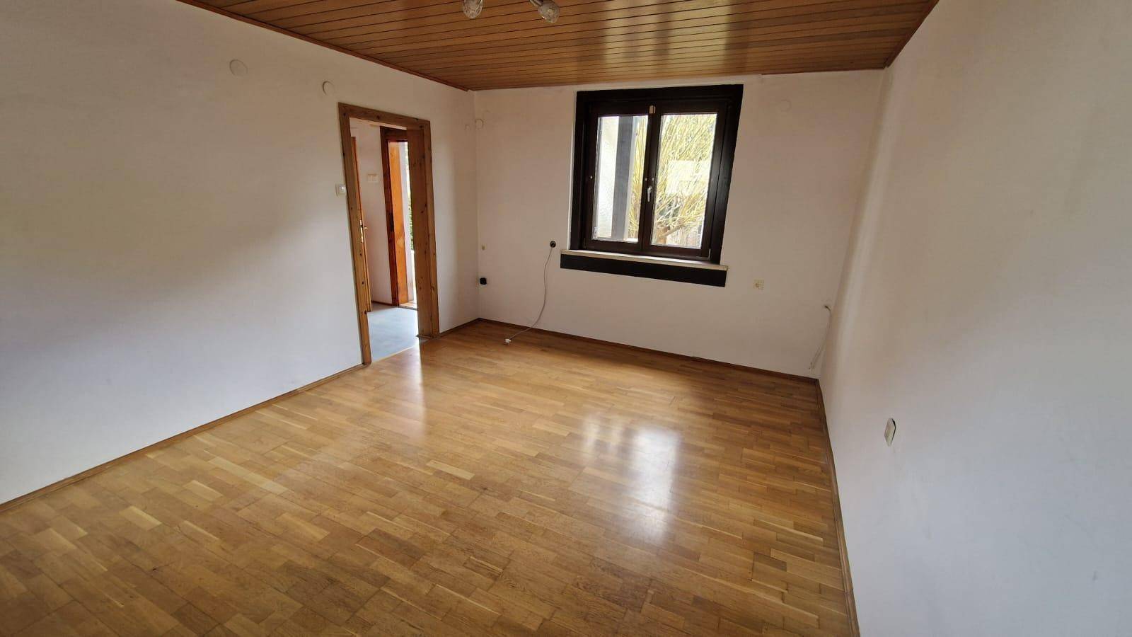 Helles Zimmer mit klassischem Holzparkettboden, weißen Wänden und einer Holzdecke.
