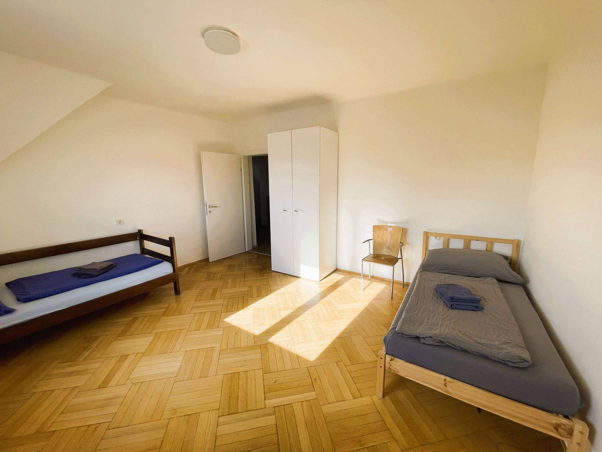 Geräumiges Schlafzimmer mit Holzparkettboden und zwei Einzelbetten, hell und freundlich.
