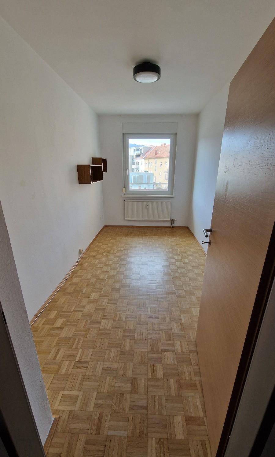 Helles Zimmer mit Parkettboden, einem Fenster und Heizkörper, bereit zur individuellen Gestaltung.