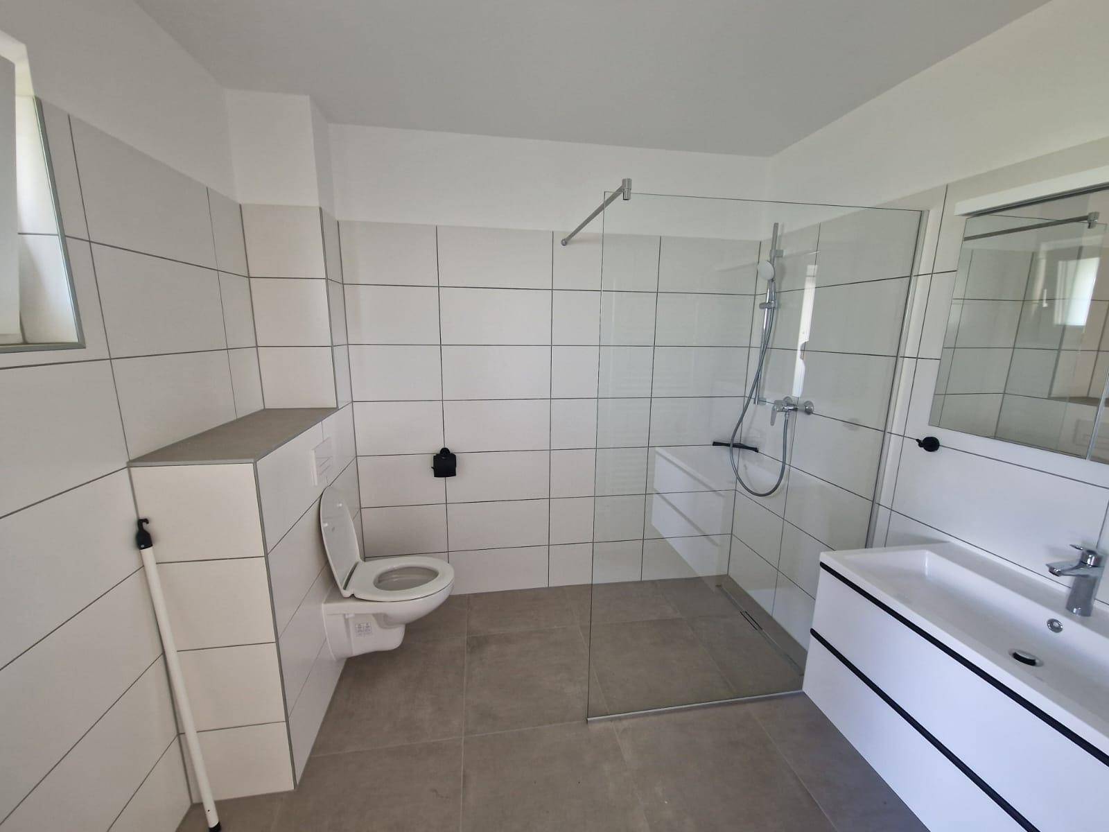 Modernes Badezimmer mit weißen Fliesen, ebenerdiger Dusche und wandhängendem WC.