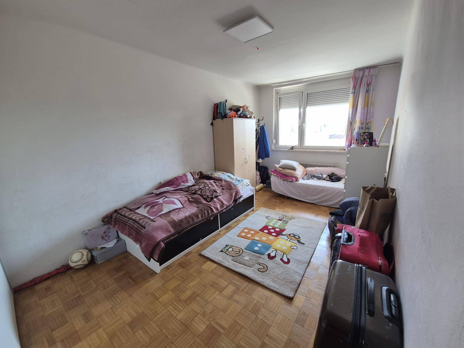 Schlafzimmer mit zwei Betten, Holzparkett und Fenster mit Rollladen.