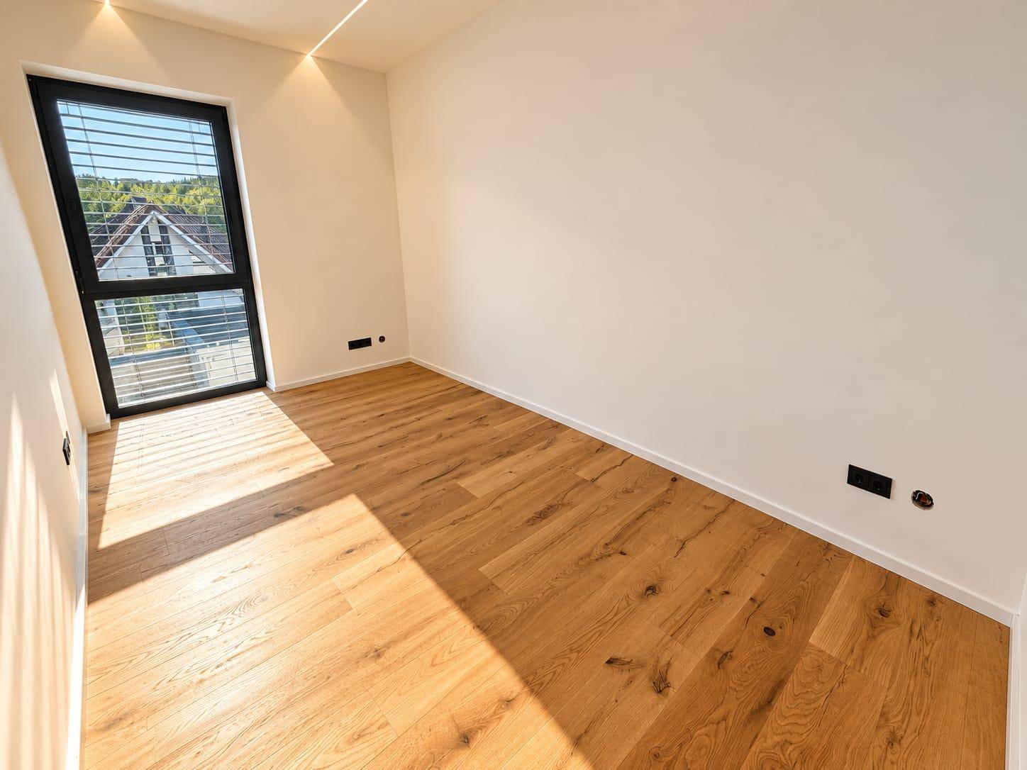 Helles Schlafzimmer mit Holzboden und großem Fenster, das einen weiten Blick nach draußen ermöglicht.