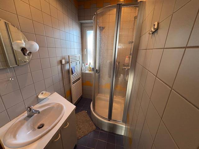 Gefliestes Badezimmer mit Duschkabine, Waschbecken und einem Fenster für natürliche Belüftung.