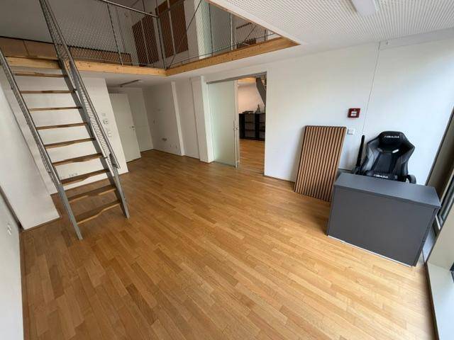 Geräumiger Wohnbereich mit Holzfußboden, einer Galerie und einem Arbeitsbereich mit modernem Stuhl.
