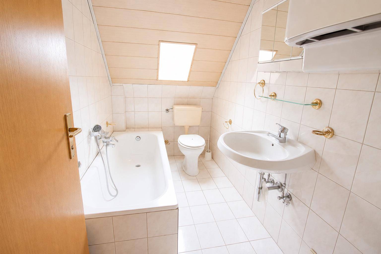 Gefliestes Badezimmer im Dachgeschoss mit Badewanne, WC, Waschbecken und Dachfenster für Tageslicht.