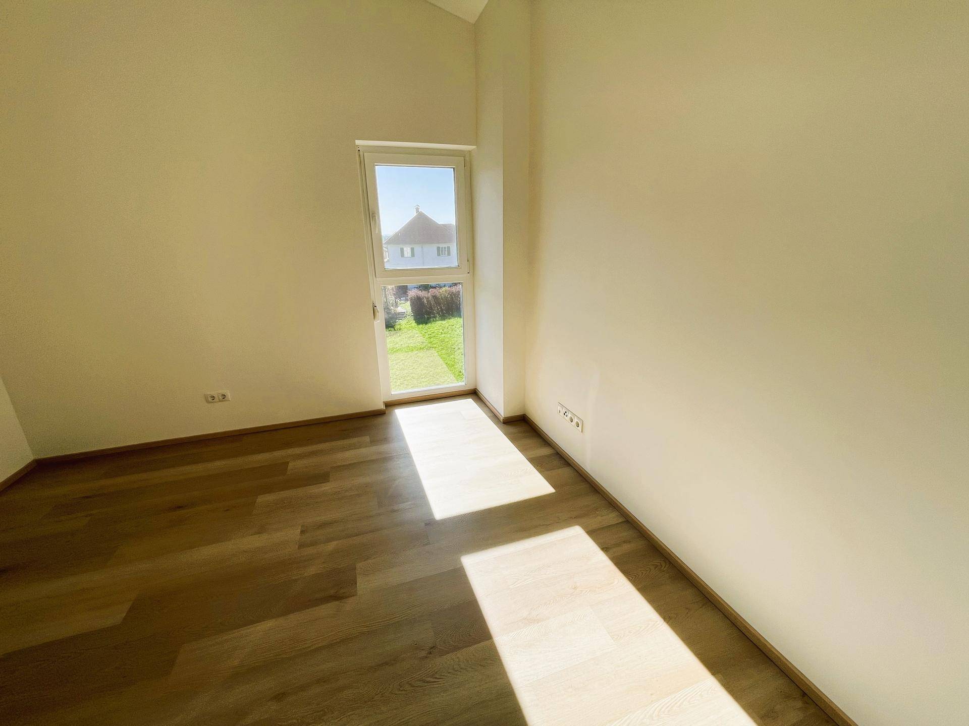 Helles Zimmer mit Holzboden und Zugang zu einem kleinen Außenbereich, durchflutet von Sonnenlicht.