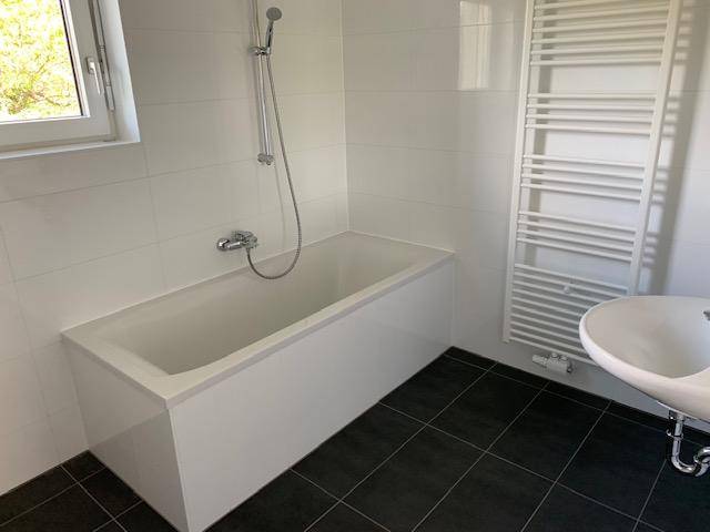 Modernes Badezimmer mit Badewanne, Duscharmatur, Waschbecken und beheiztem Handtuchhalter.