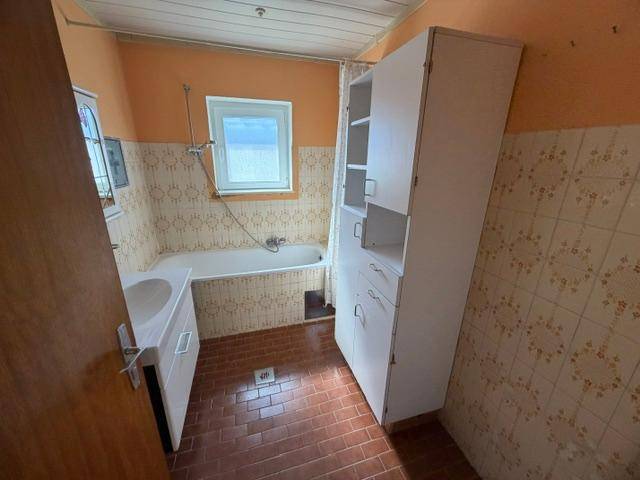 Badezimmer mit Badewanne, Waschbecken, Fenster und orangefarbenen Fliesen.