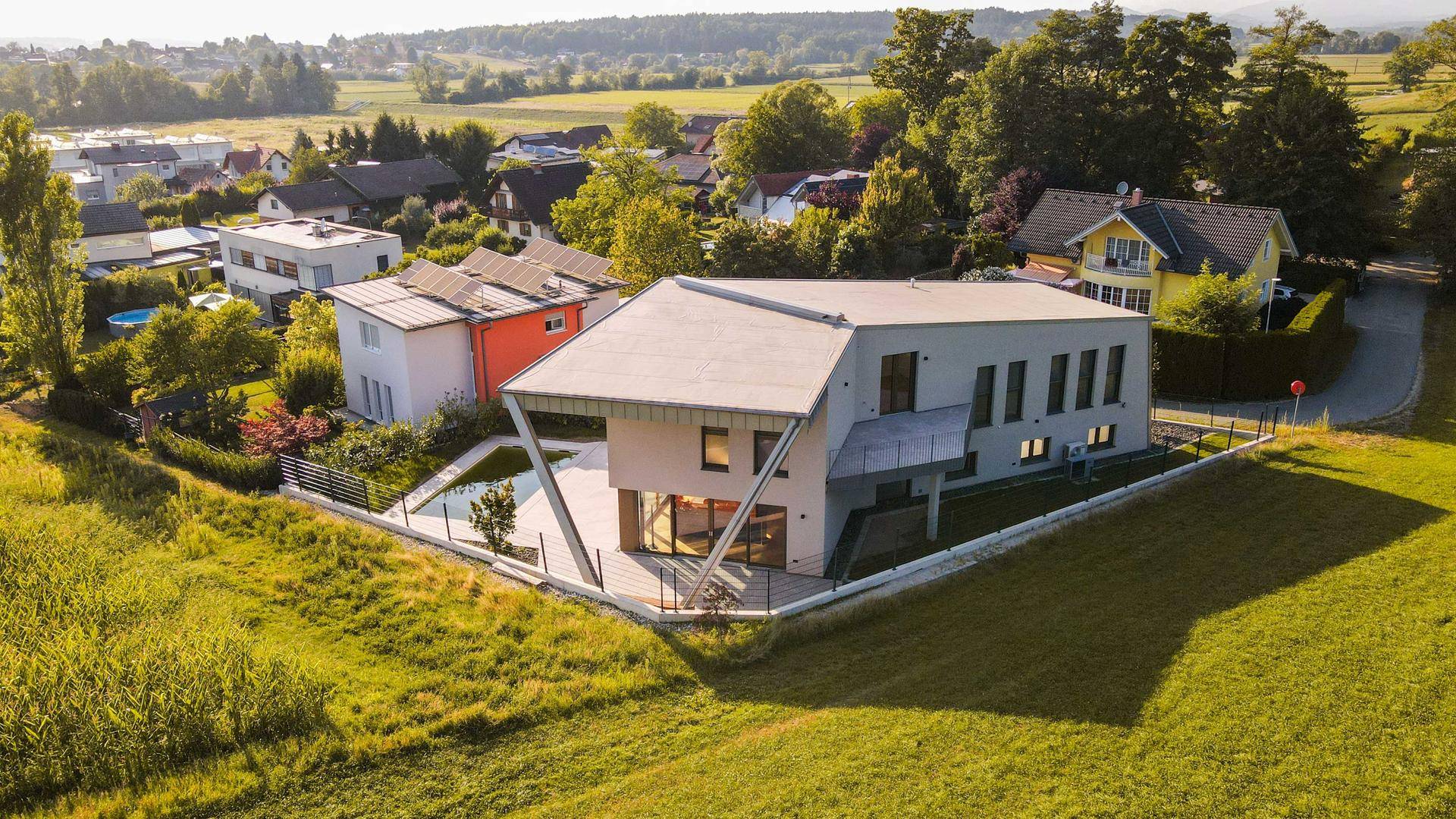 Panoramablick auf die moderne Villa und die umliegende Siedlung mit grüner Landschaft.