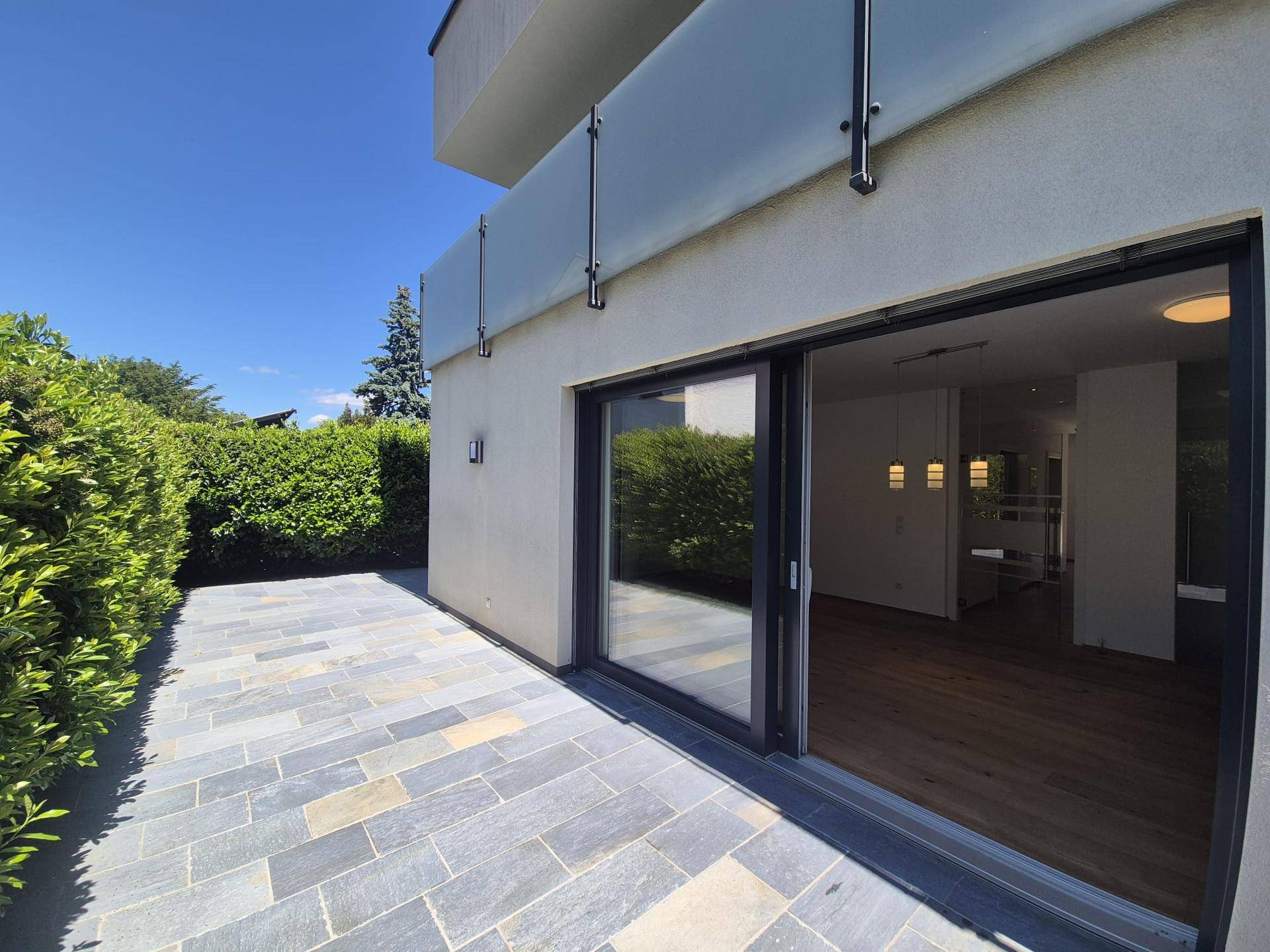 Sonniger Terrassenbereich mit Steinplatten und Hecke, ideal für entspannte Stunden im Freien.