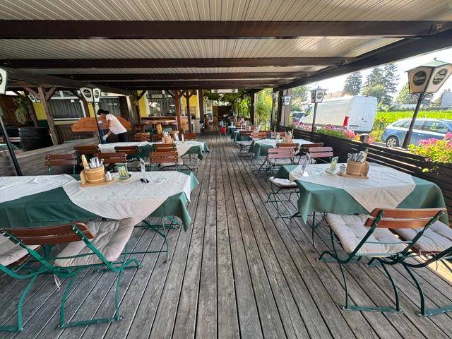 Große überdachte Holzterrasse mit zahlreichen Tischen und Stühlen für Gäste.
