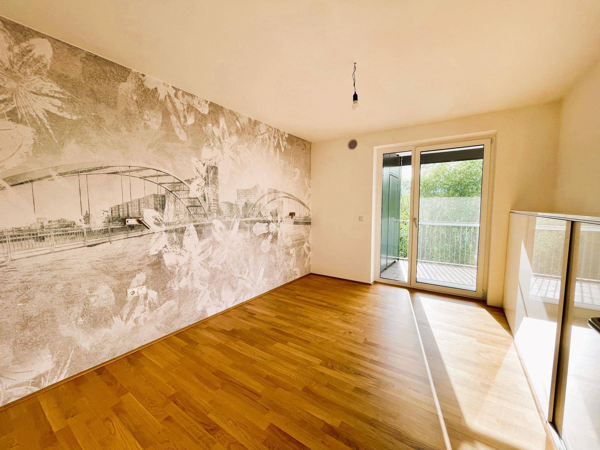 Geräumiges Zimmer mit Holzboden, dekorativer Tapete und Zugang zu einem Balkon.